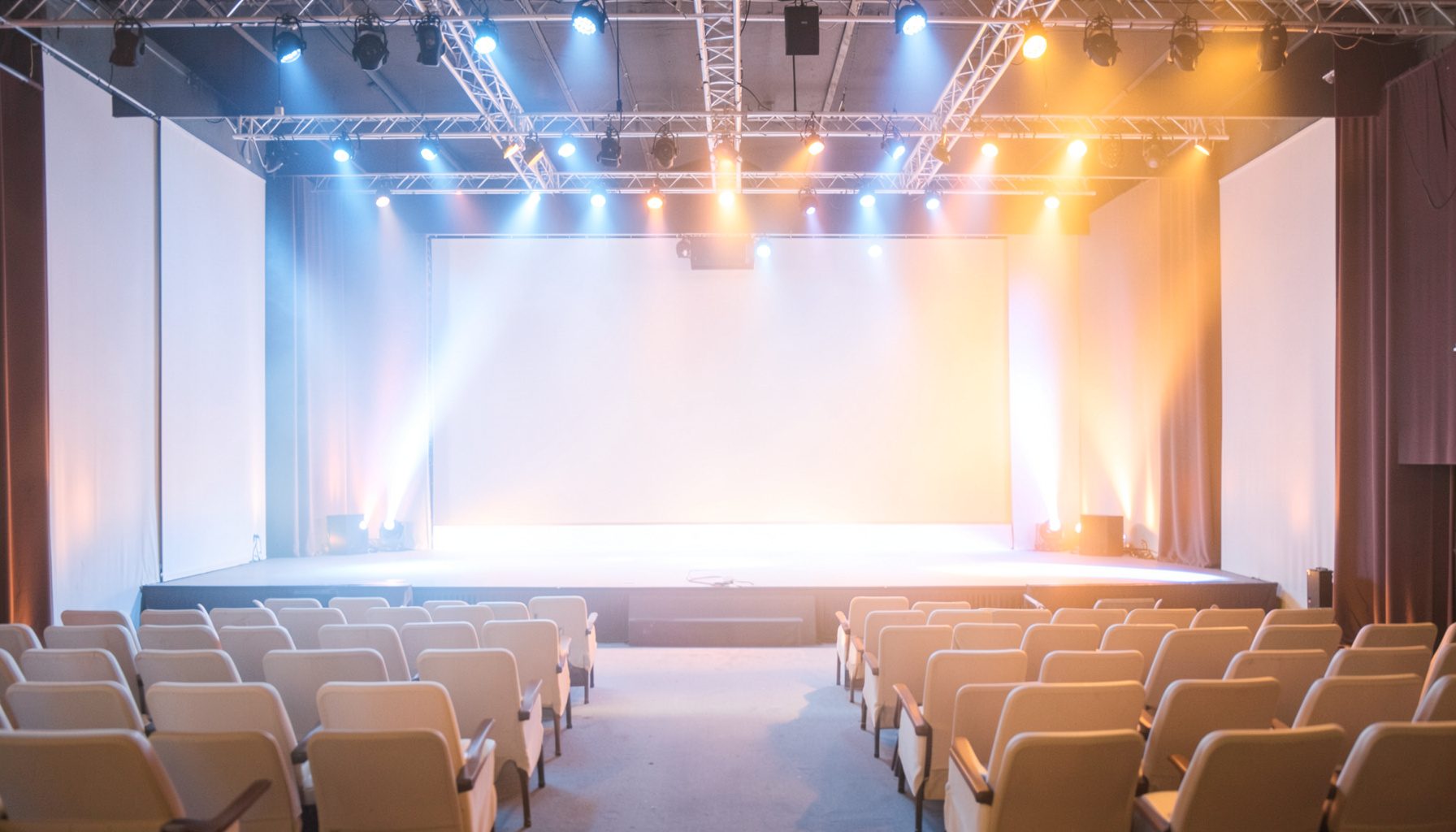 A wide shot of a conference stage with dramatic blue and amber lighting, empty seats in the foreground, conveying a prestigious awards ceremony atmosphere